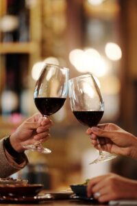 Close-up of two people toasting red wine glasses in a restaurant setting.= for anxiety in romantic relationships blog post