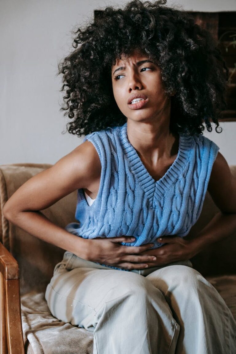 Young African American female sitting on couch at home while experiencing a churning stomach and experiencing fear of vomiting. Emetophobia: The Fear of Vomiting That Nobody Talks About