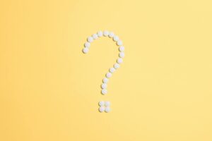 White pills arranged into a question mark shape on a vibrant yellow background.