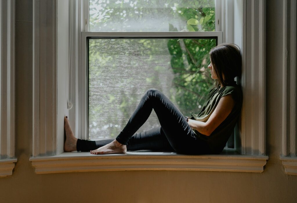 a woman sitting on a window sill contemplating mental health therapy