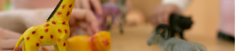 Close-up of children's hands playing with animal plastic toys representing How to Find a Play Therapist blog post.