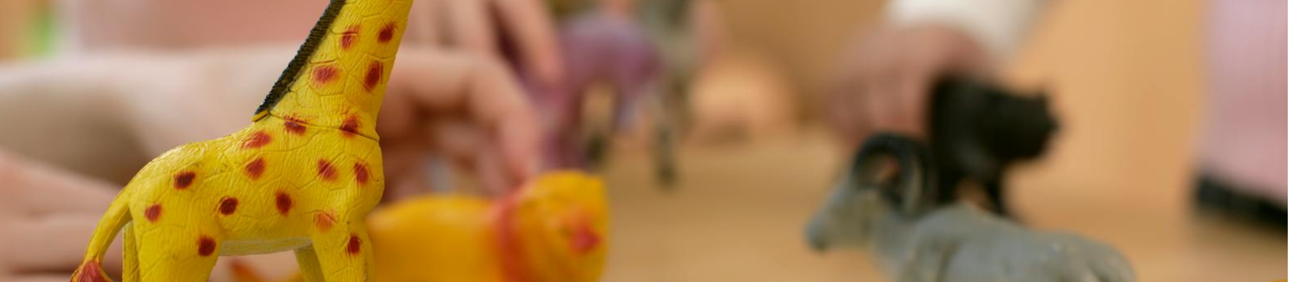 Close-up of children's hands playing with animal plastic toys representing How to Find a Play Therapist blog post.