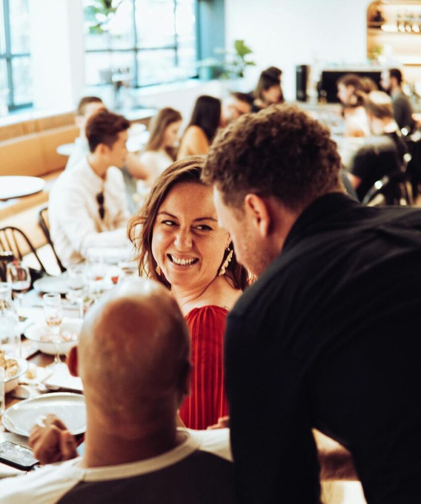 Group of friends enjoying lively conversation and dining in a restaurant setting.